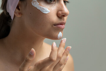 Beautiful woman looking away while applying moisturizing cream in her daily skincare routine