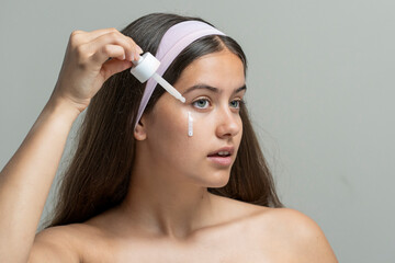 Young woman applying a milky eye serum or hydrating essence from a dropper