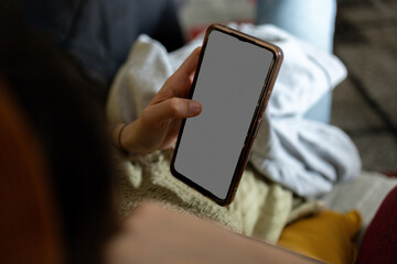 Woman relaxing on sofa using smartphone with blank screen