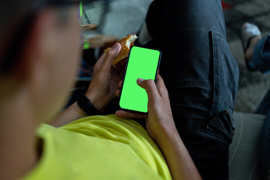 Man eating sandwich using smartphone with green screen mockup