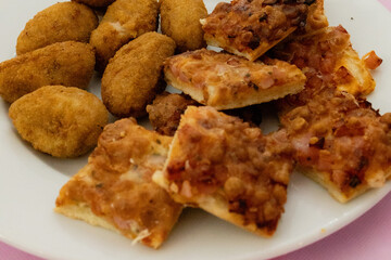 Delicious breaded chicken croquettes and sliced pizza resting on white plate