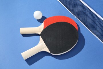 Ping pong rackets, ball and net on blue background, closeup