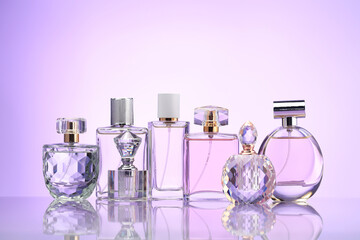 Bottles of perfume on mirror surface against pale violet gradient background