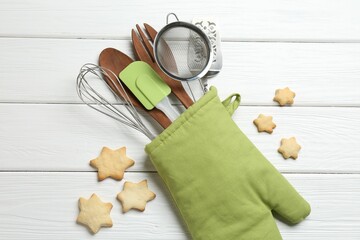 Different kitchen utensils in oven mitten and star shaped cookies on white wooden table, flat lay