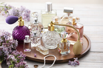 Bottles of perfumes, accessories and lilac flowers on white wooden table