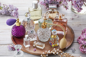 Bottles of perfumes, accessories and lilac flowers on white wooden table