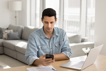 Focused young male remote working professional specialist freelancer multitasking between texting...
