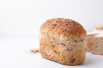 Freshly baked loaf of bread with sesame seeds on light table, closeup. Space for text