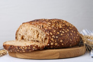 Freshly baked loaf of bread with oat flakes on light table against grey background, closeup