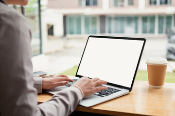 A desk in front of a window with a white laptop screen mockup on it.