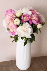 Bouquet of beautiful peonies in vase on wooden table near beige wall indoors