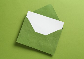 Blank invitation card and envelope on green background, top view