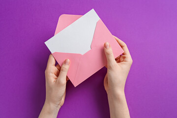 Woman holding envelope with blank invitation card on purple background, top view