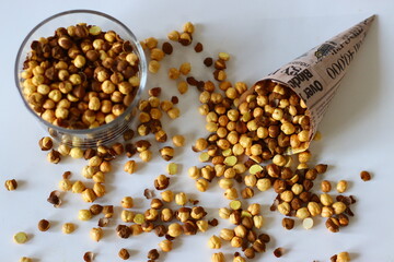 Crispy Roasted Channa chickpeas in a glass and in newspaper cone, scattered on white background