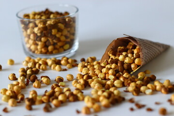 Crispy Roasted Channa chickpeas in a glass and in newspaper cone, scattered on white background