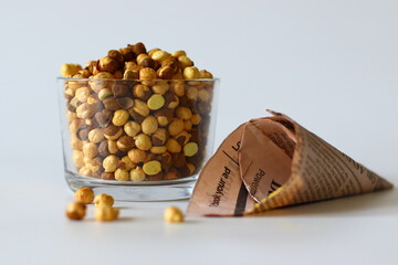 Crispy Roasted Channa chickpeas in a glass and in newspaper cone, scattered on white background