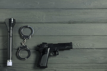 Police equipment. Gun, handcuffs and flashlight on grey wooden table, flat lay. Space for text