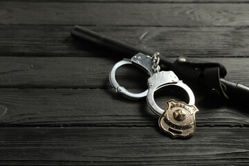 Police badge, handcuffs and baton on black wooden table, closeup. Space for text