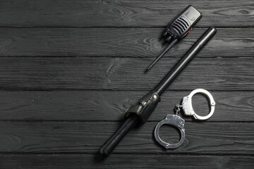 Police baton, walkie talkie and handcuffs on black wooden table, flat lay. Space for text