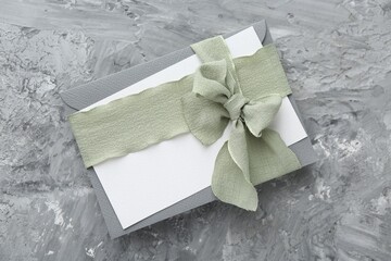 Blank invitation card, ribbon and envelope on grey textured table, top view