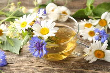 Aromatic herbal tea in glass cup and flowers on wooden table, closeup