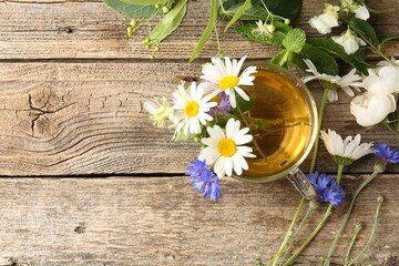 Aromatic herbal tea in glass cup, flowers and green leaves on wooden table, flat lay. Space for text