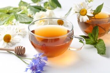 Aromatic herbal tea in glass cups, different flowers and mint on white background, closeup