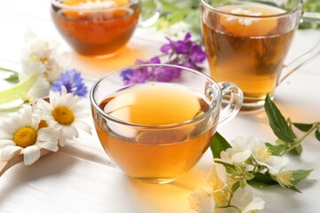 Aromatic herbal tea in glass cups and different flowers on white wooden table, closeup