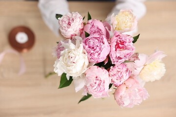 Florist with beautiful bouquet of peonies at table, top view
