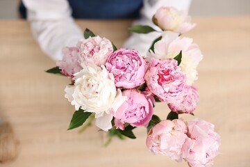 Florist with beautiful bouquet of peonies at table, top view