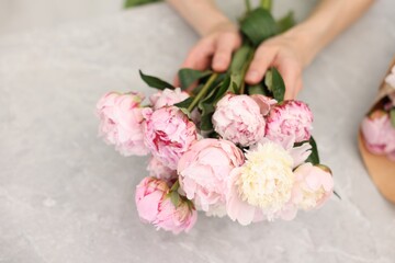 Florist making beautiful bouquet of peonies at grey marble table, closeup