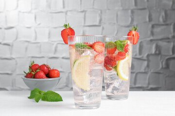 Tasty refreshing drink with strawberries, lemon and mint on white table