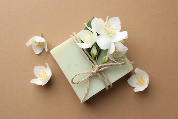Soap bar and jasmine flowers on light brown background, flat lay