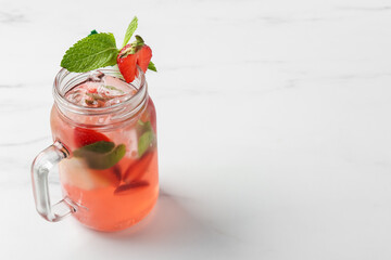Refreshing drink with strawberries, ice and mint in mason jar on white table, closeup. Space for text