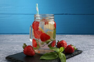 Refreshing drink with strawberries and mint on grey textured table against blue wooden background, closeup