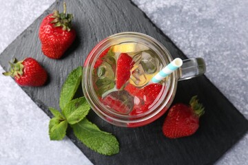 Refreshing drink with strawberries, lemon, ice and mint on grey textured table, top view
