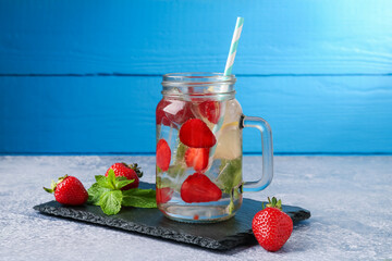 Refreshing drink with strawberries, lemon and mint on grey textured table against blue wooden...