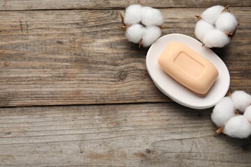 Soap bar and cotton flowers on wooden table, flat lay. Space for text