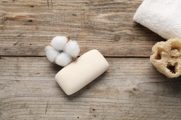 Soap bar, towel, loofah sponge and cotton flowers on wooden table, flat lay