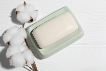 Soap bar and cotton flowers on white wooden table, flat lay