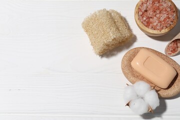 Soap bar, sea salt, cotton flower and loofah on white wooden table, flat lay. Space for text
