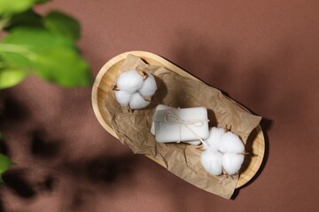 Soap bars and cotton flowers on brown background, top view