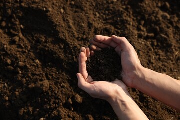 Man holding pile of soil in field, top view. Space for text