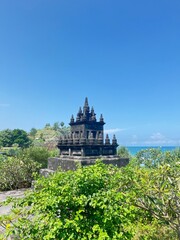 Majestic Stone Temple by the Sea: This image captures the imposing presence of a stone temple against the backdrop of a bright blue sky and the sea. Lush green plants frame the ancient structure.