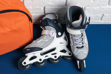 Pair of roller skates and backpack on blue table near white brick wall, above view