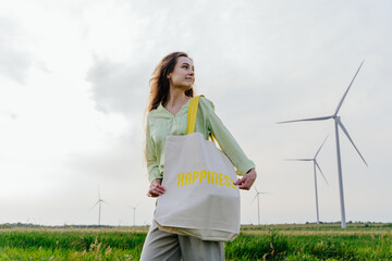 Woman in field holding reusable tote bag with happiness slogan