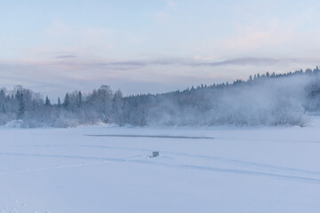 Serene winter landscape featuring a frozen lake surrounded by snow-covered trees and mist, creating a tranquil atmosphere with soft pastel hues in the sky