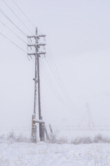 Power lines stand tall against a snowy landscape, surrounded by a blanket of white snow, creating a...