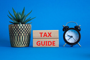 Tax Guide symbol. Concept word Tax Guide on Beautiful blue background with alarm clock and...