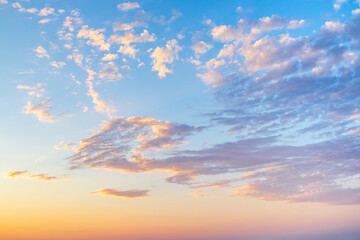 sky with wispy cirrus clouds illuminated by the setting sun in soft orange tones. Celestial landscape